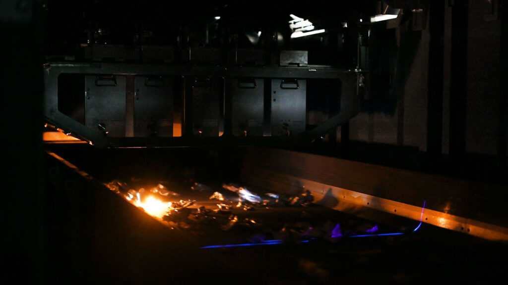 Dark interior of the sorting system where laser pulses create bright plasma sparks on aluminum scrap pieces moving along the conveyor belt