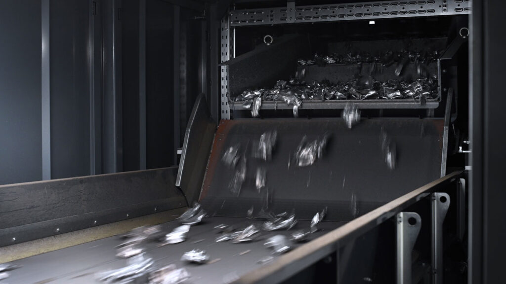 Shredded aluminum scrap pieces falling from a feeder onto the conveyor belt inside the sorting system