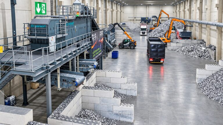 Recycling hall at OSR with a Cleansort LIBS sorting system on a steel platform, conveyors discharging sorted aluminum scrap into concrete bays, and excavators and trucks handling scrap piles