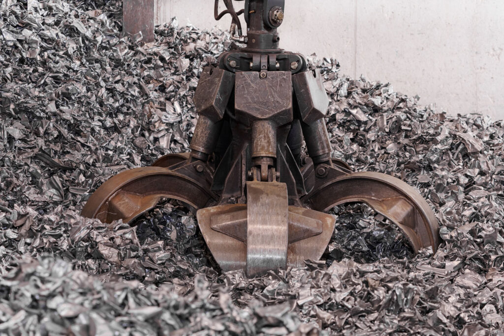 Hydraulic orange-peel grab digging into a large pile of shredded aluminum automotive scrap