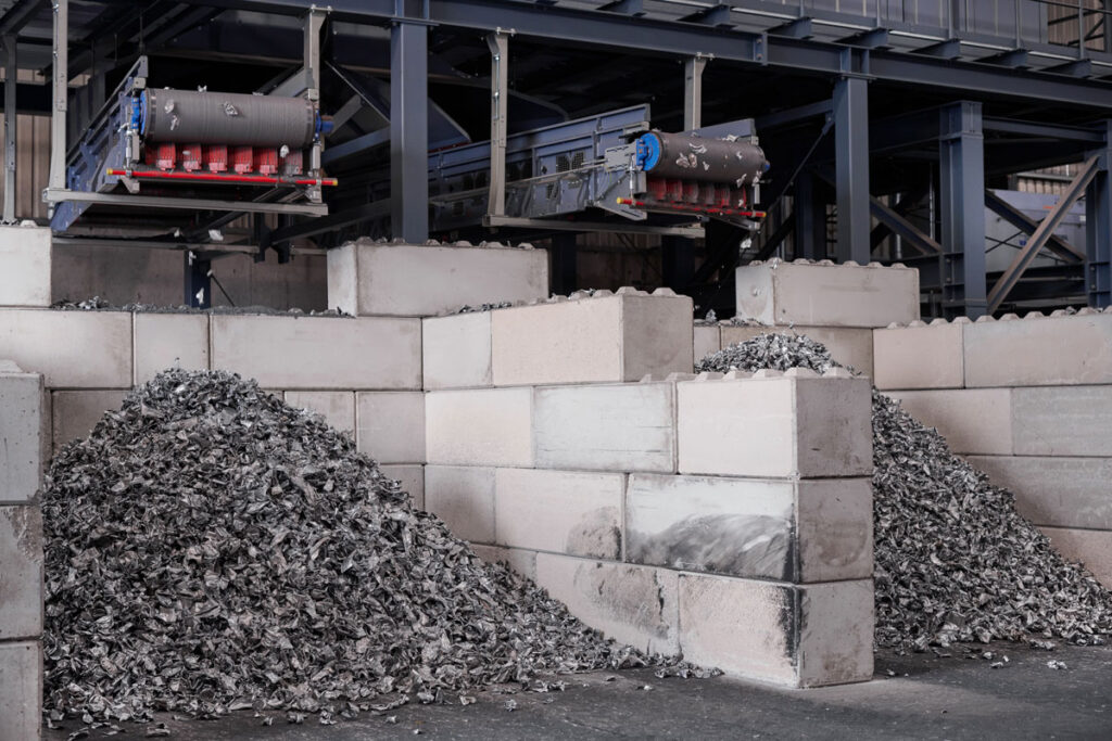 Two discharge conveyors above concrete block bays filled with piles of sorted shredded aluminum scrap