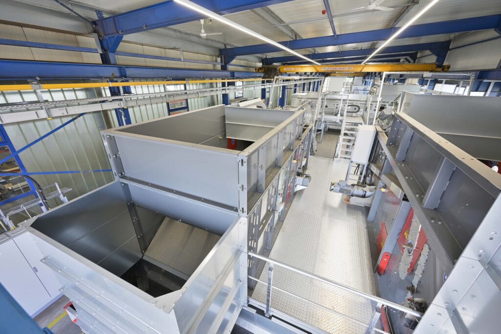 High-angle view of galvanized steel equipment, a hopper, walkways with chequer plate and a ladder under blue steel roof beams