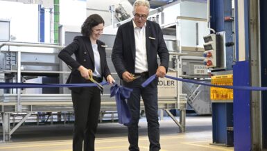 Julia Stadler and Willi Stadler cutting a blue ribbon with golden scissors in front of sorting equipment in the new Test Center
