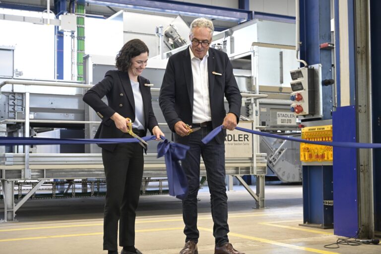 Julia Stadler and Willi Stadler cutting a blue ribbon with golden scissors in front of sorting equipment in the new Test Center