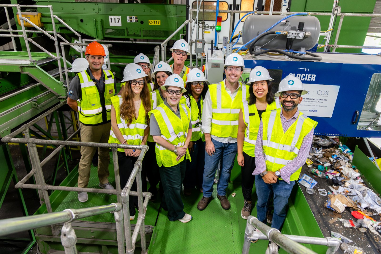 Group of people in hi-vis vests and hard hats standing on the sorting platform next to the Glacier AI-powered recycling robot at the Circular Services MRF in Sarasota