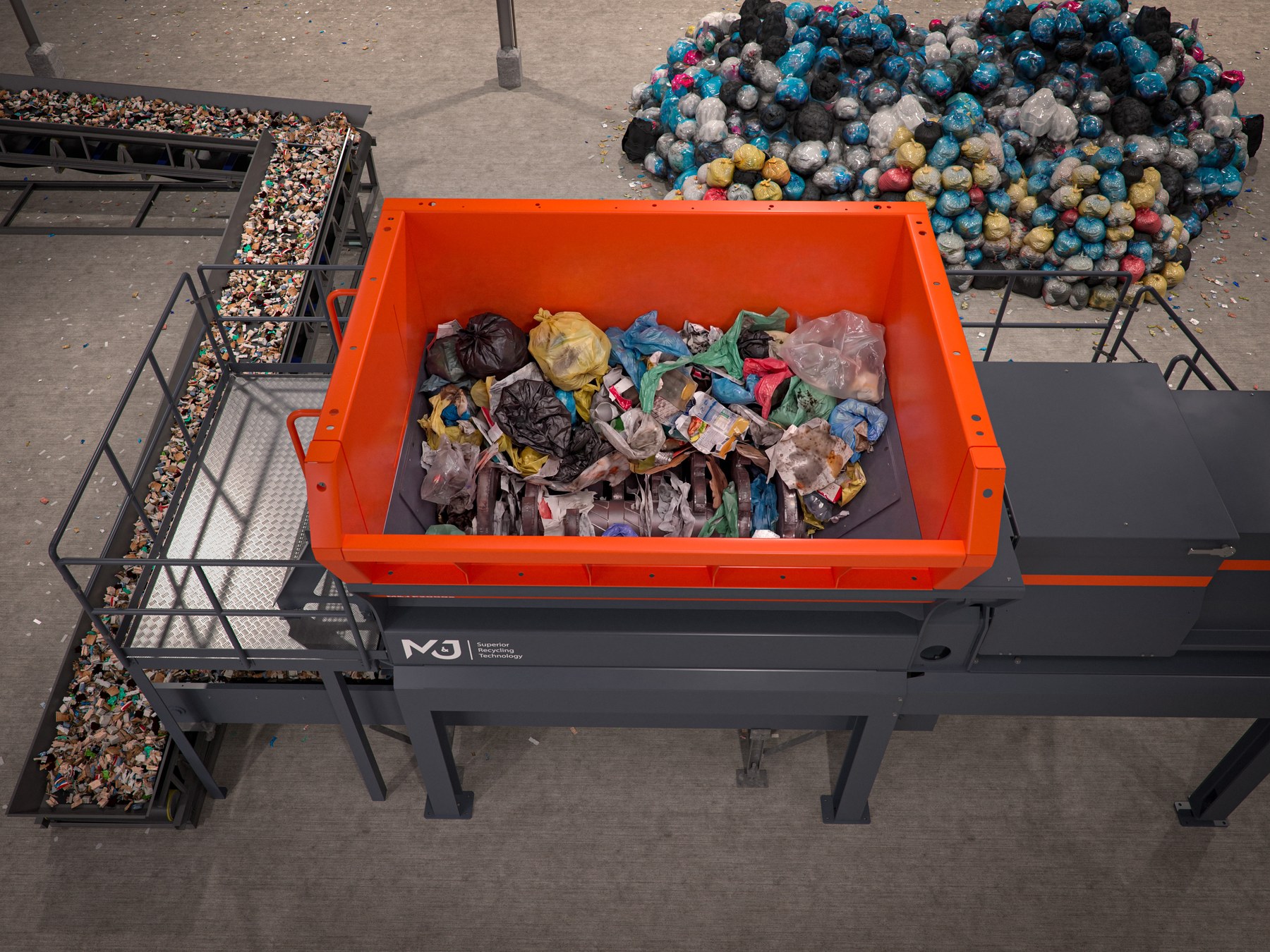 Top-down view into the orange feed hopper of the M&J P2000e electric pre-shredder, filled with household waste bags and packaging above the single shredding shaft