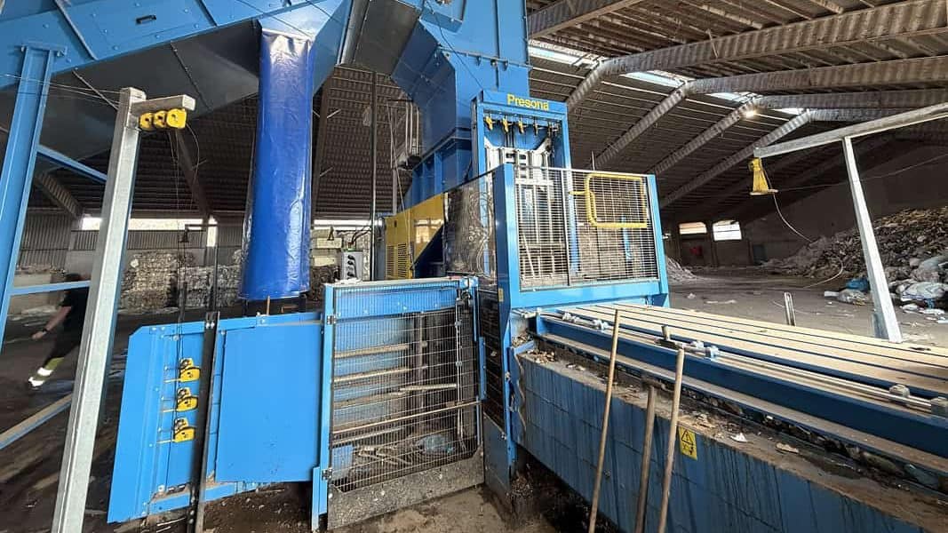 Bale outlet and wire-tying unit of a blue Presona channel baler next to a bale conveyor