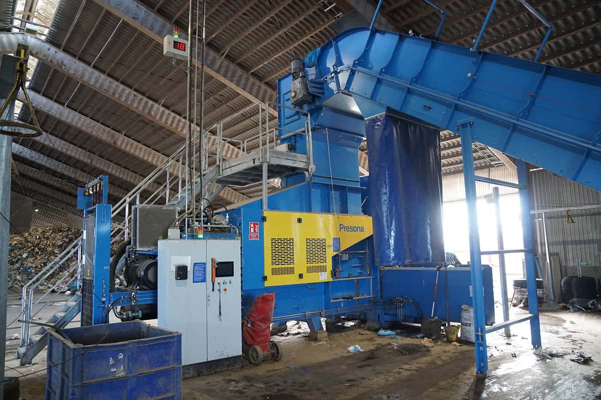 Blue Presona prepress baler with an inclined infeed conveyor and control cabinet inside a recycling hall