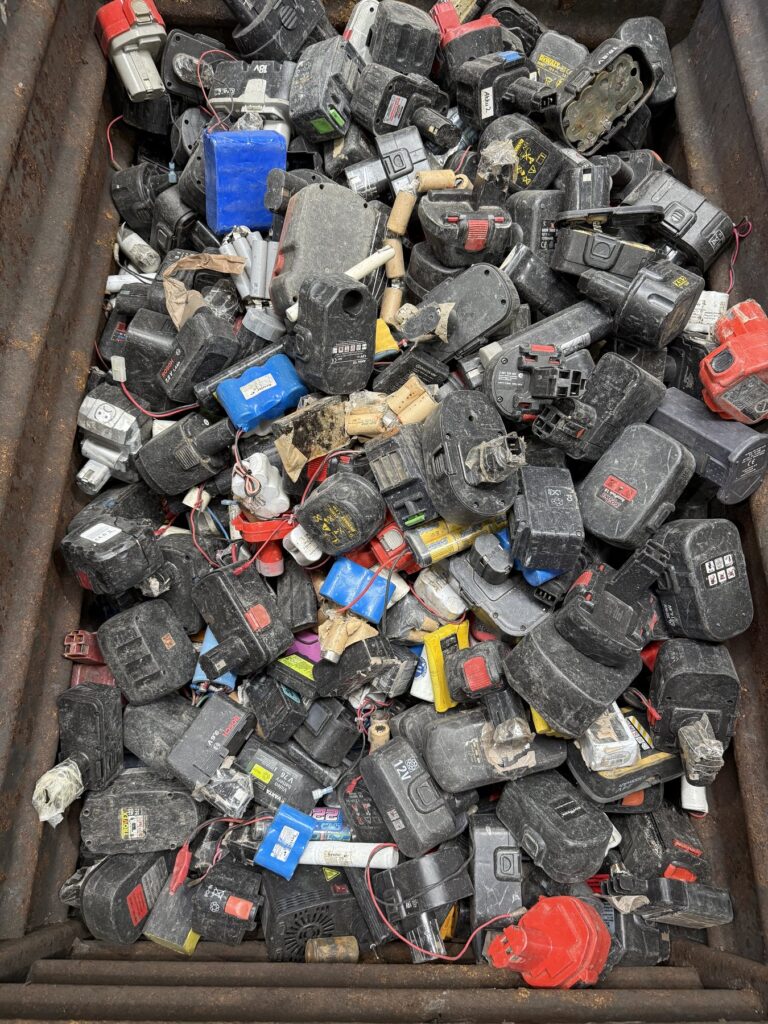 Steel bin filled with used rechargeable battery packs from cordless power tools in black, red and blue casings