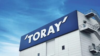 White industrial building with a large blue Toray sign on the roof edge and an exterior fire escape staircase against a blue sky