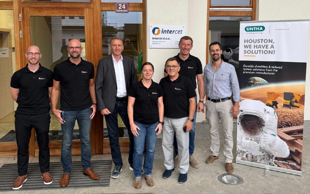 Seven team members of Intercet and UNTHA standing in front of the Intercet d.o.o. office entrance next to an UNTHA roll-up banner