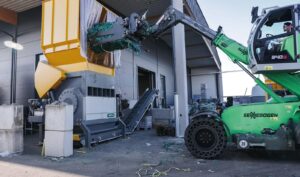 UNTHA MR1800C PRO single-shaft shredder with yellow feed hopper being loaded with film bales by a green material handler at RDG-Plast
